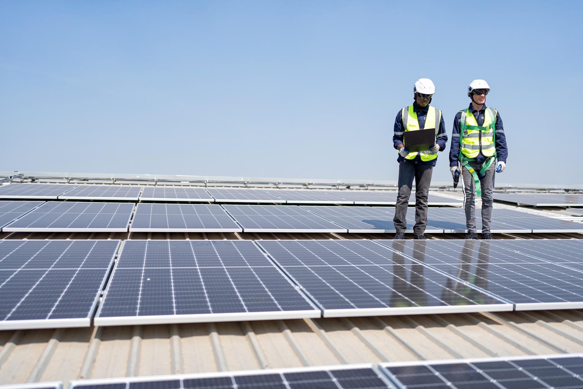 engineer-on-rooftop-stand-next-to-solar-panels-discussion-with-team-check-laptop-for-installation.jpg